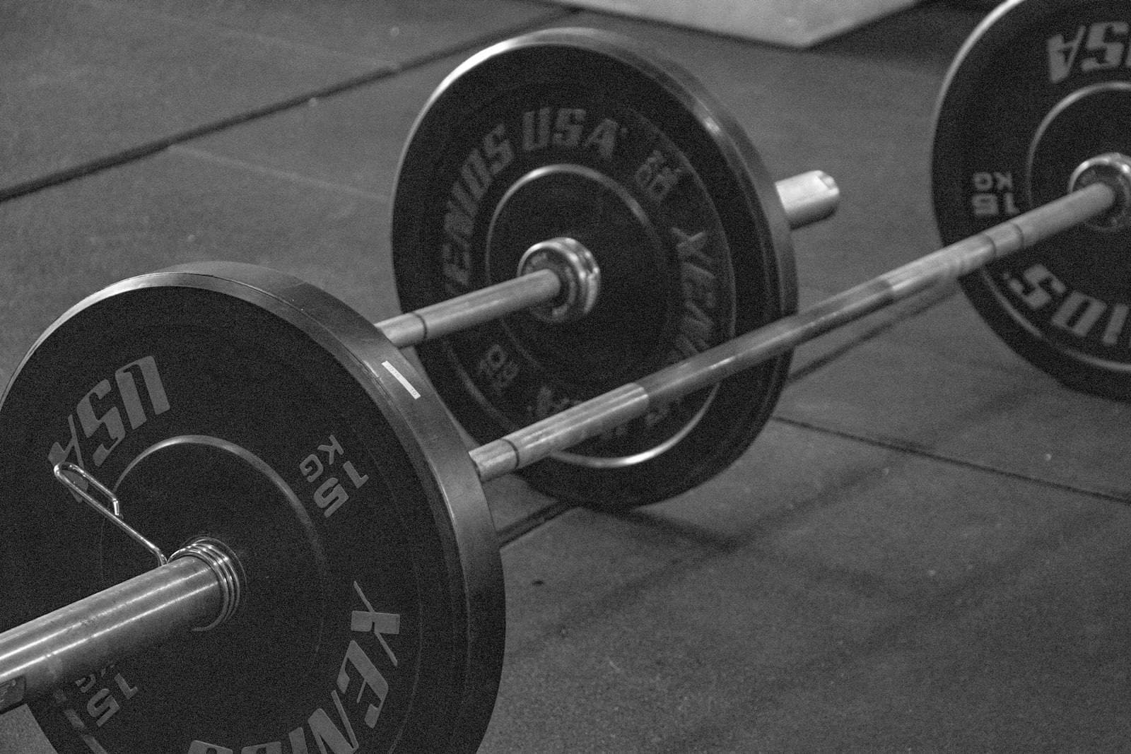 A loaded barbell resting on a gym floor, in black and white